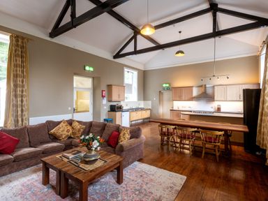 An open plan living room and kitchen with a brown sofa and wooden dining table at The Old School in Gortin