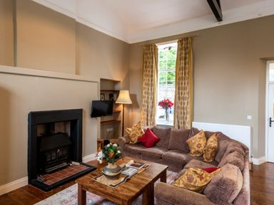 A sitting room with a fireplace a wooden coffee table and a sectional sofa with cushions at The Old School in Gortin