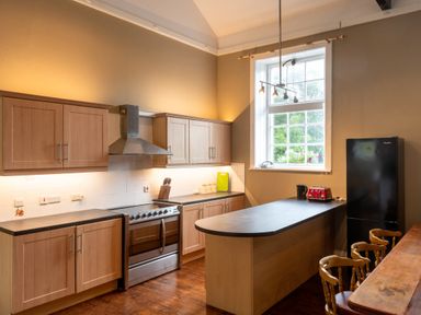 A kitchen with wooden cabinets a black refrigerator a stove an island with a toaster and kettle a wooden dining table and chairs and a window at The Old School in Gortin