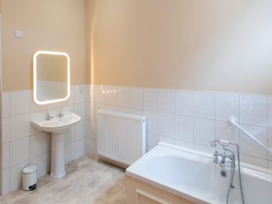 A bathroom with a pedestal sink a mirror with light a radiator and a bathtub at The Old School in Gortin