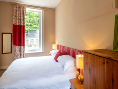 A bedroom with a bed a bedside table with lamp a window with curtains and a wooden wardrobe at The Old School in Gortin