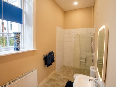 A bathroom with a sink toilet shower area with glass partition mirror with light and window with blue blind at The Old School in Gortin