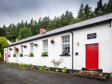 A white building with red doors and flower pots on windowsills surrounded by trees at The Old School in Gortin