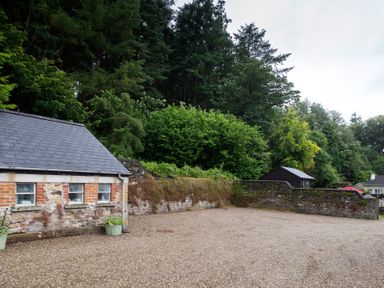 An outdoor area with a gravel ground next to a stone and brick building and a stone wall with trees in the background at The Old School in Gortin