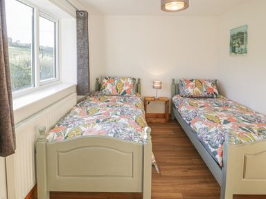 A bedroom with two single beds with floral bedding a wooden nightstand with a lamp a window and curtains at Isallt in Rhostryfan near Bontnewydd Gwynedd