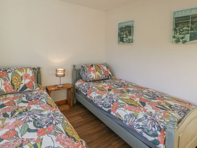 A bedroom with two single beds with floral bedding and a wooden nightstand with a lamp between the beds at Isallt in Rhostryfan near Bontnewydd Gwynedd