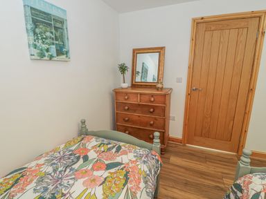 A bedroom with floral bedding a wooden dresser with a mirror and a wooden door at Isallt in Rhostryfan near Bontnewydd Gwynedd
