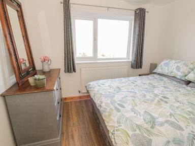 A bedroom with a bed and patterned bedding near a window with curtains and a dresser with a mirror and plants at Isallt in Rhostryfan near Bontnewydd Gwynedd