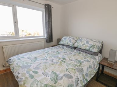 A bedroom with a bed with leaf patterned bedding and two bedside tables with lamps at Isallt in Rhostryfan near Bontnewydd Gwynedd