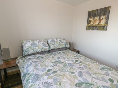 A bedroom with a bed with leaf patterned bedding and two bedside tables with lamps and a painting of owls on the wall at Isallt in Rhostryfan near Bontnewydd Gwynedd