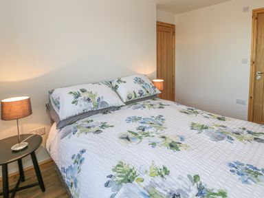 A bedroom with a bed covered in floral bedding two bedside tables with lamps and wooden doors at Isallt in Rhostryfan near Bontnewydd Gwynedd