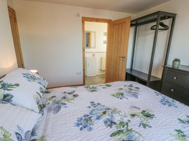 A bedroom with a floral bedspread a wooden door a black wardrobe and a black chest of drawers at Isallt in Rhostryfan near Bontnewydd Gwynedd