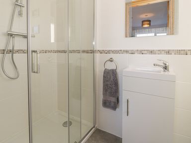 A bathroom with a glass shower enclosure and a white vanity unit with a sink and a gray towel hanging on a ring at Isallt in Rhostryfan near Bontnewydd Gwynedd