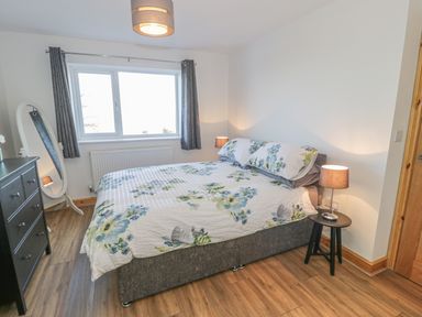A bedroom with a double bed covered in floral bedding two bedside lamps a black chest of drawers and a standing oval mirror at Isallt in Rhostryfan near Bontnewydd Gwynedd