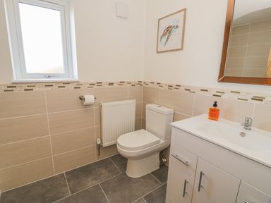 A bathroom with a toilet a sink with cabinet a mirror a window and a framed picture at Isallt in Rhostryfan near Bontnewydd Gwynedd