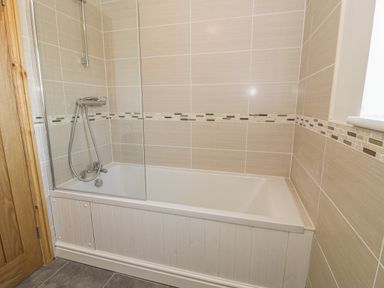 A bathroom with a bathtub shower combination with tiled walls and a wooden door at Isallt in Rhostryfan near Bontnewydd Gwynedd