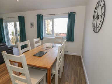 A dining room with a wooden table and white chairs next to windows and a large wall clock at Isallt in Rhostryfan near Bontnewydd Gwynedd