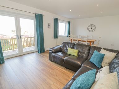 A living room with a black leather sofa blue curtains and a wooden dining table at Isallt in Rhostryfan near Bontnewydd Gwynedd
