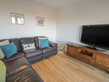 A living room with a brown leather sofa and wooden TV stand with a flat screen TV at Isallt in Rhostryfan near Bontnewydd Gwynedd