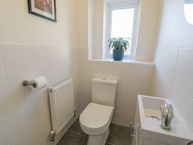 A small bathroom with a toilet sink radiator and a plant on the window sill at Isallt in Rhostryfan near Bontnewydd Gwynedd