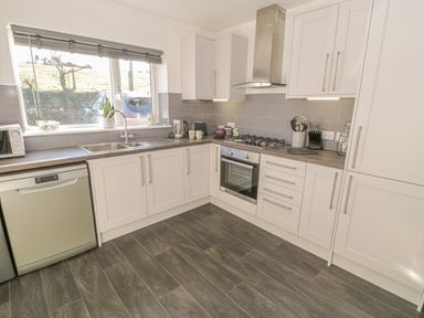 A kitchen with white cabinets a dishwasher a sink a gas stove oven and kitchen utensils at Isallt in Rhostryfan near Bontnewydd Gwynedd