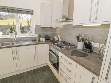 A kitchen with white cabinets gray tiled backsplash and wood countertops at Isallt in Rhostryfan near Bontnewydd Gwynedd