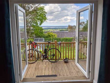 A balcony with a bike and a helmet looking out to a garden and distant landscape at Isallt in Rhostryfan near Bontnewydd Gwynedd