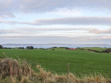 A green field with grass and a fence in the foreground and water and hills in the background at Woodleigh Cottage in Ballycastle