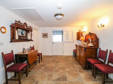 A room with wooden chairs, a wooden cabinet with a lamp, a wooden drop-leaf table, and a white door at Woodleigh Cottage in Ballycastle