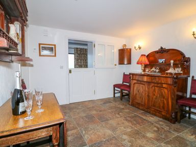 A room with wooden furniture including a sideboard table and chairs with a bottle and glasses on the table at Woodleigh Cottage in Ballycastle