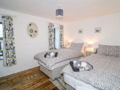A bedroom with two beds with patterned bedding wooden floor and bedside tables with lamps at Woodleigh Cottage in Ballycastle