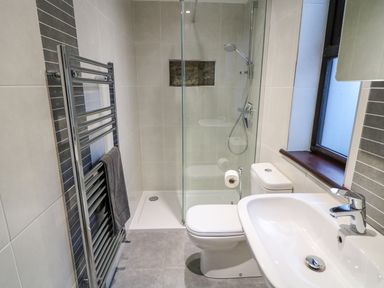 A bathroom with a shower cubicle toilet sink and towel rack at Woodleigh Cottage in Ballycastle