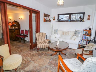 A living room with various chairs a white sofa a round wooden table and a bookshelf at Woodleigh Cottage in Ballycastle