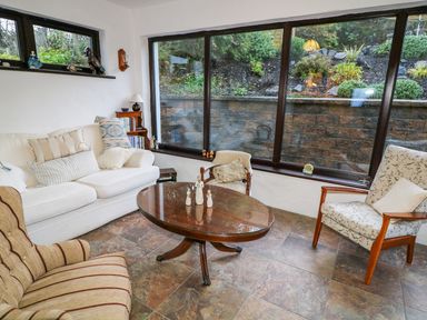 A sitting area with sofa armchairs and a wooden coffee table in front of large windows at Woodleigh Cottage in Ballycastle