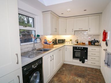 A kitchen with white cabinets a black oven a washing machine and various kitchen items on countertops at Woodleigh Cottage in Ballycastle