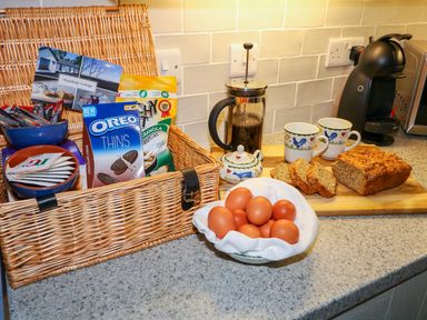 A kitchen counter with a wicker basket of snacks a bowl of eggs a coffee press two mugs and sliced bread at Woodleigh Cottage Ballycastle