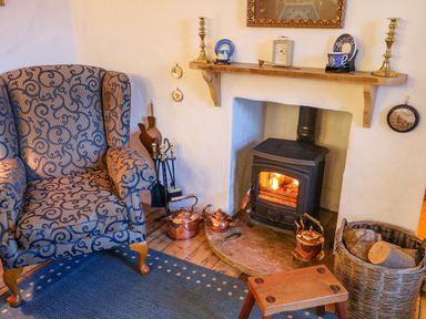 An armchair next to a fireplace with a wood stove and a basket of firewood at Woodleigh Cottage in Ballycastle
