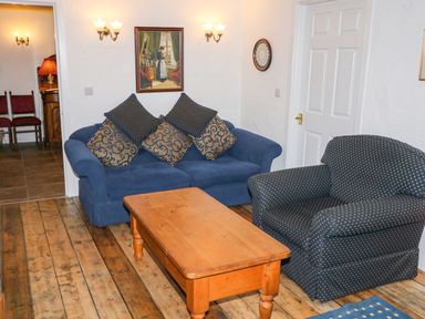 A living room with blue sofa and armchair a wooden coffee table and wall painting at Woodleigh Cottage in Ballycastle
