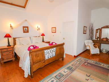 A bedroom with a wooden bed and nightstands with lamps and a dresser with a mirror at Woodleigh Cottage in Ballycastle