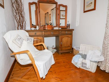 A wooden dressing table with three mirrors and a chair covered with white fabric in a room at Woodleigh Cottage in Ballycastle