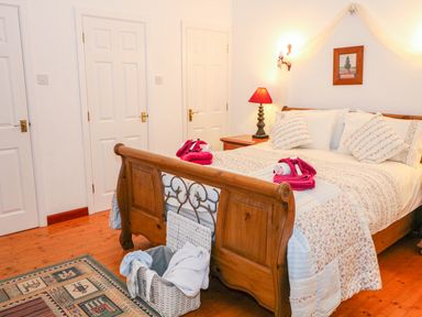 A bedroom with a wooden bed with patterned bedding a bedside table with a lamp and a basket on a wooden floor at Woodleigh Cottage in Ballycastle