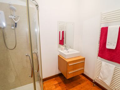 A bathroom with a corner shower cubicle a wall-mounted wooden vanity unit with a basin and a mirror and a heated towel rail with towels at Woodleigh Cottage in Ballycastle