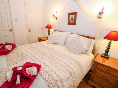 A bedroom with a double bed and floral bedding two bedside tables with lamps and doors in the background at Woodleigh Cottage in Ballycastle