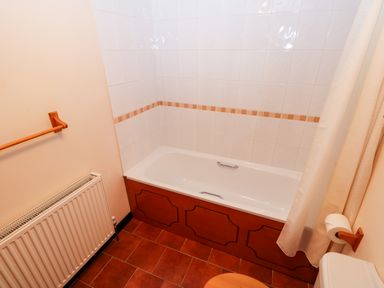 A bathroom with a bathtub with wood paneling a towel rack a radiator and a toilet with toilet paper at Hitchens Cottage in Happisburgh