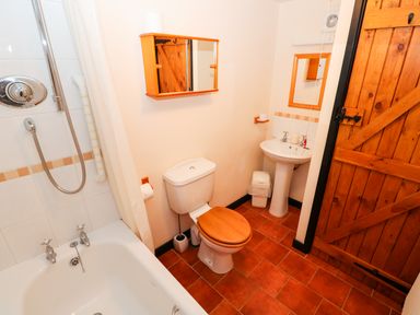 A bathroom with a bathtub shower combination a toilet a sink and a wooden door at Hitchens Cottage in Happisburgh