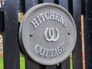 A round metal sign with horseshoes and the text Hitchens Cottage on a black wooden fence at Hitchens Cottage in Happisburgh