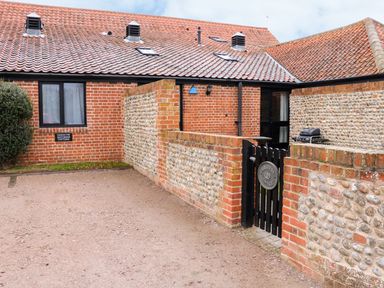Exterior view of a brick and flint cottage with a tiled roof a small black gate and a parking area at Hitchens Cottage in Happisburgh
