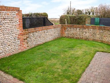A small grassy garden area enclosed by a low brick and flint wall with a paved path at Hitchens Cottage in Happisburgh