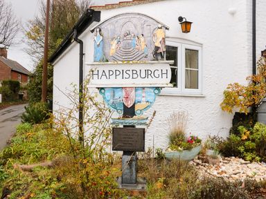A village sign with the name Happisburgh in front of a white house with a window and garden Happisburgh