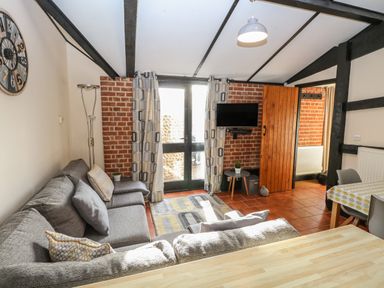 A living room with a grey sofa a wall clock and a small wall mounted television at Hitchens Cottage in Happisburgh